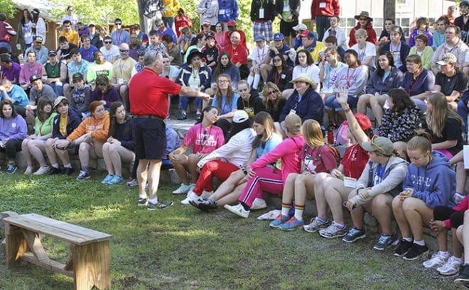 Bishop David Talley, fourth row back, center, sits among the campers as Deacon Bob Brunton of St. Thomas Aquinas Church, Alpharetta, foreground, standing left center, leads a moment of prayer and reflection in the amphitheater before morning activities begin at the 2015 Toni’s Camp. Photo By Michael Alexander