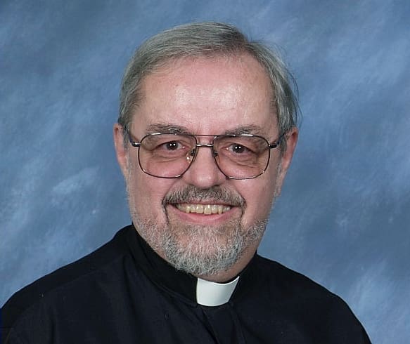 Father James H. Sexstone is photographed, smiling.