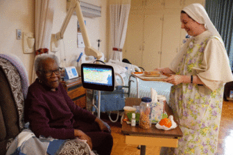 Sister Bernadette, a Dominican Sister of Hawthorne, serves lunch to Mary, a patient at Our Lady of Perpetual Help Home. The home, supported solely by voluntary donations from the public, is a free home for those with incurable cancers or other diseases. Photo by Julianna Leopold